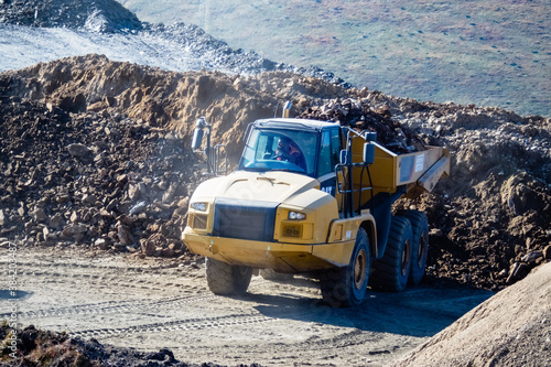 Heavy duty machine at work. Construction site high in the mountains. Big yellow truck carrying heavy loads of materials.