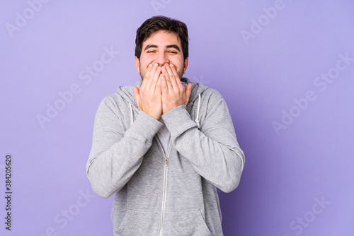 Young man isolated on purple background laughing about something, covering mouth with hands.