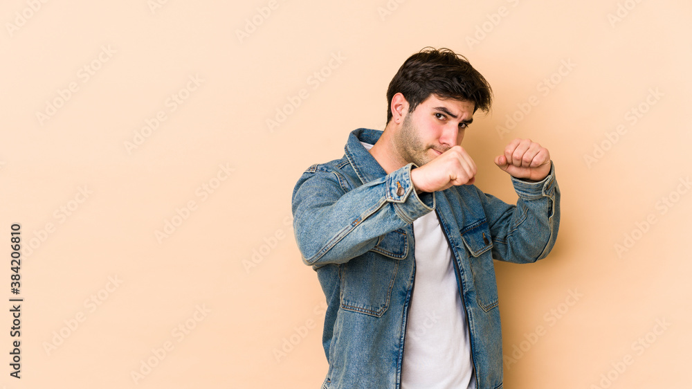Young man isolated on beige background throwing a punch, anger, fighting due to an argument, boxing. Young man isolated on beige background throwing a punch, anger, fighting due to an argument, boxing.