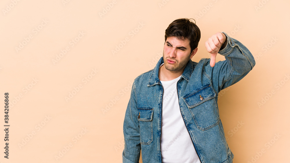 Young man isolated on beige background showing thumb down and expressing dislike. Young man isolated on beige background showing thumb down and expressing dislike.