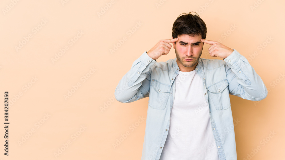 Young man isolated on beige background focused on a task, keeping forefingers pointing head. Young man isolated on beige background focused on a task, keeping forefingers pointing head.