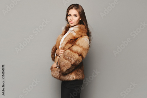 Side view of a model girl in a luxurious fur coat at the grey background. Winter fashion