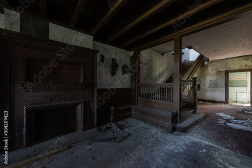 This is an interior view of the first-floor foyer with a brick fireplace and stunning wood-paneled staircase at the long-abandoned and historic Dunnington Mansion in Farmville  Virginia.