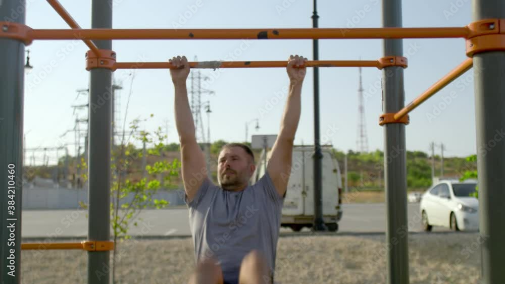 Senior sporty man hangs on a horizontal bar and raises his legs Senior sporty man hangs on a horizontal bar and raises his legs