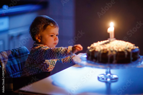 Cute beautiful little baby girl celebrating first birthday. Child blowing one candle on homemade baked cake, indoor. Birthday family party for lovely toddler child, beautiful daughter