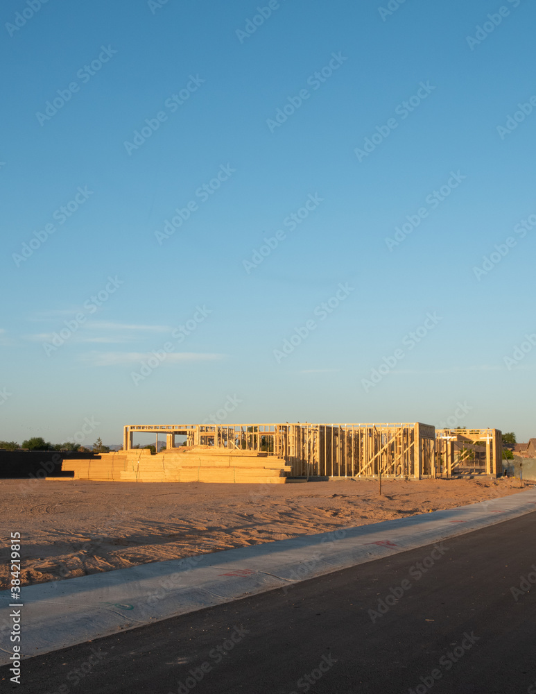Wooden frame of a single house on a dirt lot showing only the timber walls before siding and roof in early morning light in a horizontal view of the lot. Wooden frame of a single house on a dirt lot showing only the timber walls before siding and roof in early morning light in a horizontal view of the lot.