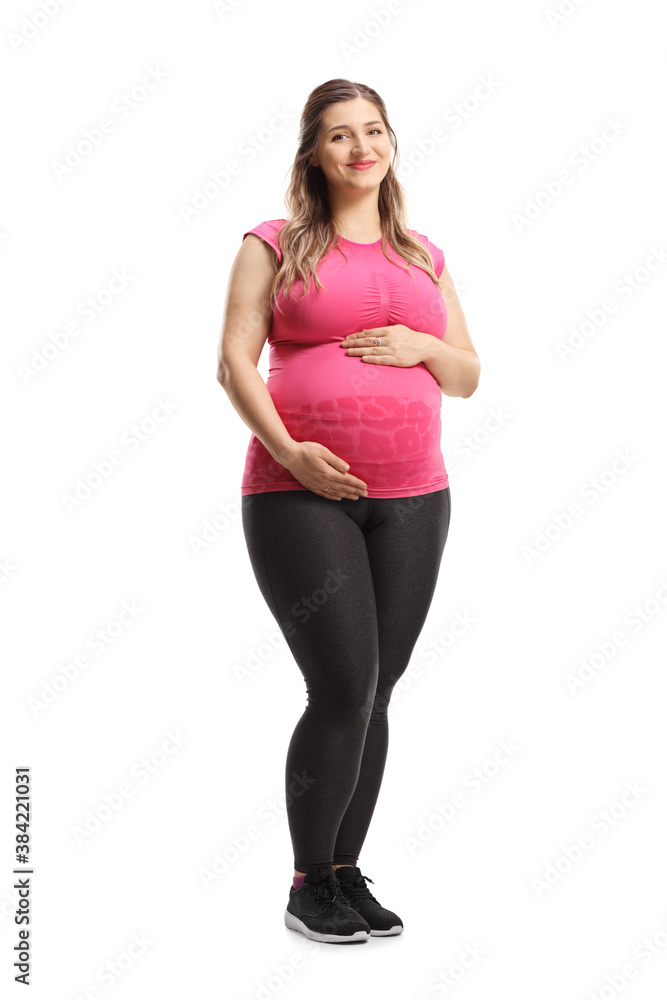 Full length portrait of a pregnant woman in pink top and leggings smiling and holding her belly Full length portrait of a pregnant woman in pink top and leggings smiling and holding her belly