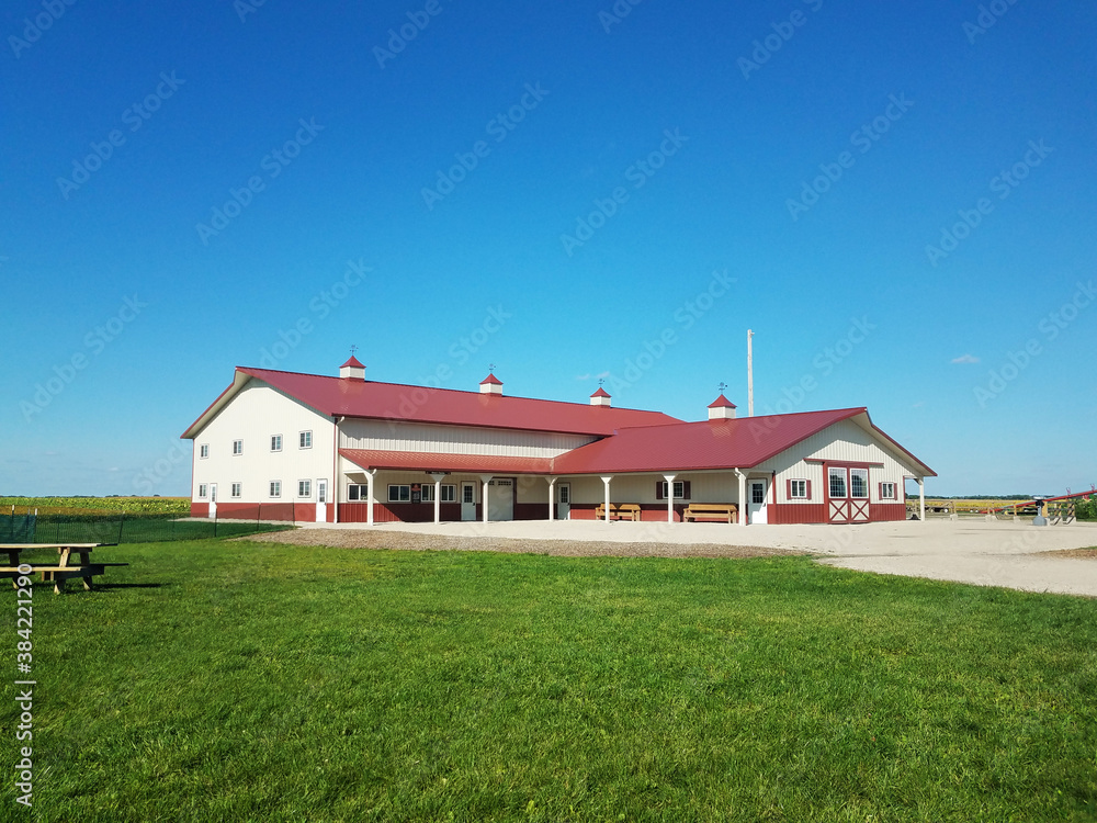 Red roof barn on the farm, with a bright blue sky in the background and lush green grass in the front