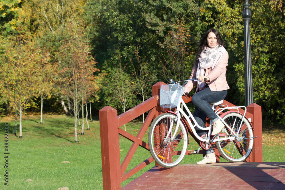 Girl on a bike ride in the autumn park. Crossing a wooden bridge with a bicycle in his hands.
