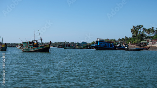 Several traditional wooden boats and houses on the shore of Chaung Thar, Myanmar