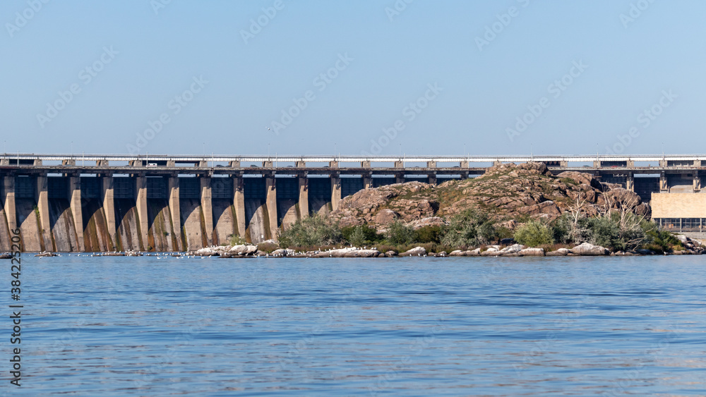 Dneproges with rocks in water of Dnieper river on sunny day. Hydro electric power plant in Zaporozhye, Ukraine. View from Khortytsia island