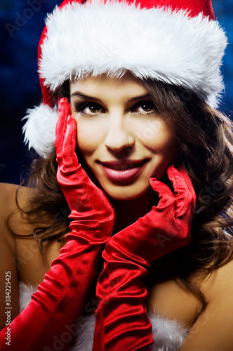 Portrait of young woman with happy smile in Santa costume. Beautiful girl with red gloves on dark blue background