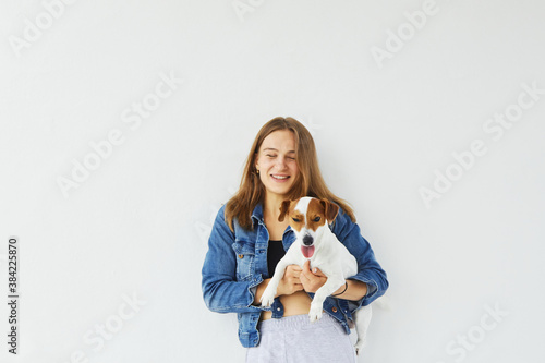 Young cheerful caucasian woman in a denim jacket is holding her pet, jack russell terrier, and is smiling with her eyes closed. Dog is looking into the camera with his tongue out. On white background. © Stanislava