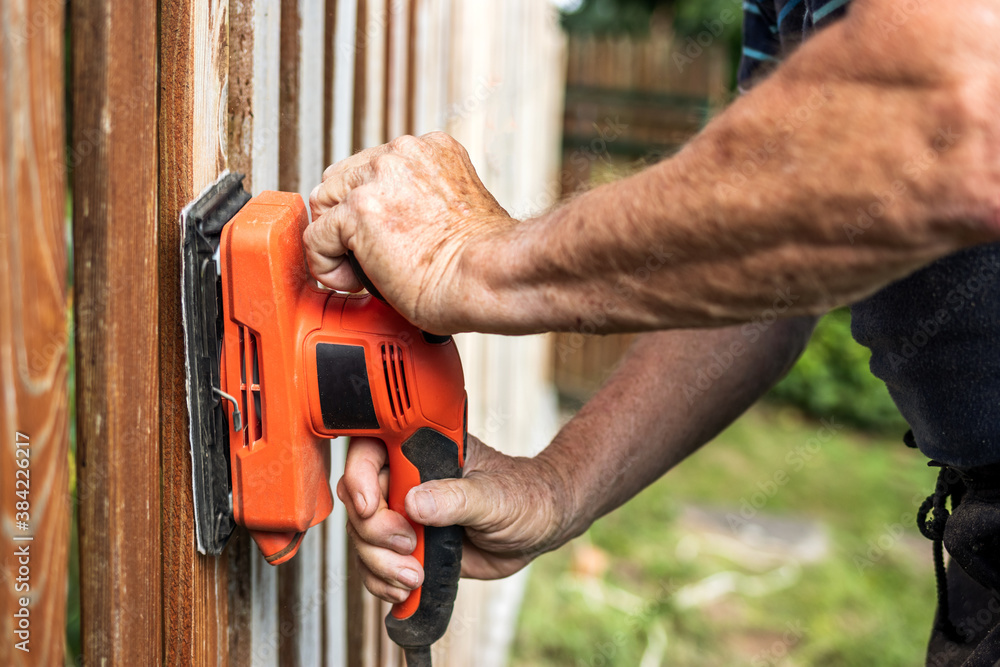 Sanding wood. Close-up sander in hands. Repairing wooden fence Sanding wood. Close-up sander in hands. Repairing wooden fence