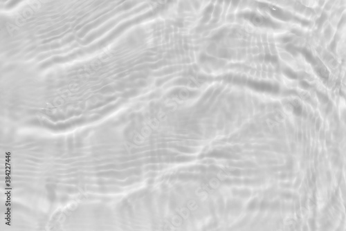 Subtle white texture of light-shadow pattern of sunlight reflection from rippled water surface. Beautiful natural wallpaper. Grayscale calm water waves.