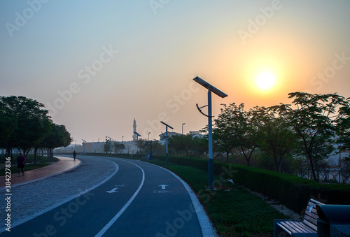 Jogging and cycling tracks in the park early in the morning. Lamp post powered by solar panels can be seen in the picture as well as minaret of a mosque.
