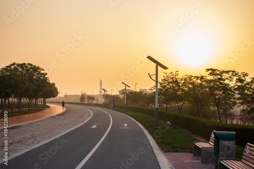Jogging and cycling tracks in the park early in the morning. Lamp post powered by solar panels can be seen in the picture as well as minaret of a mosque.
