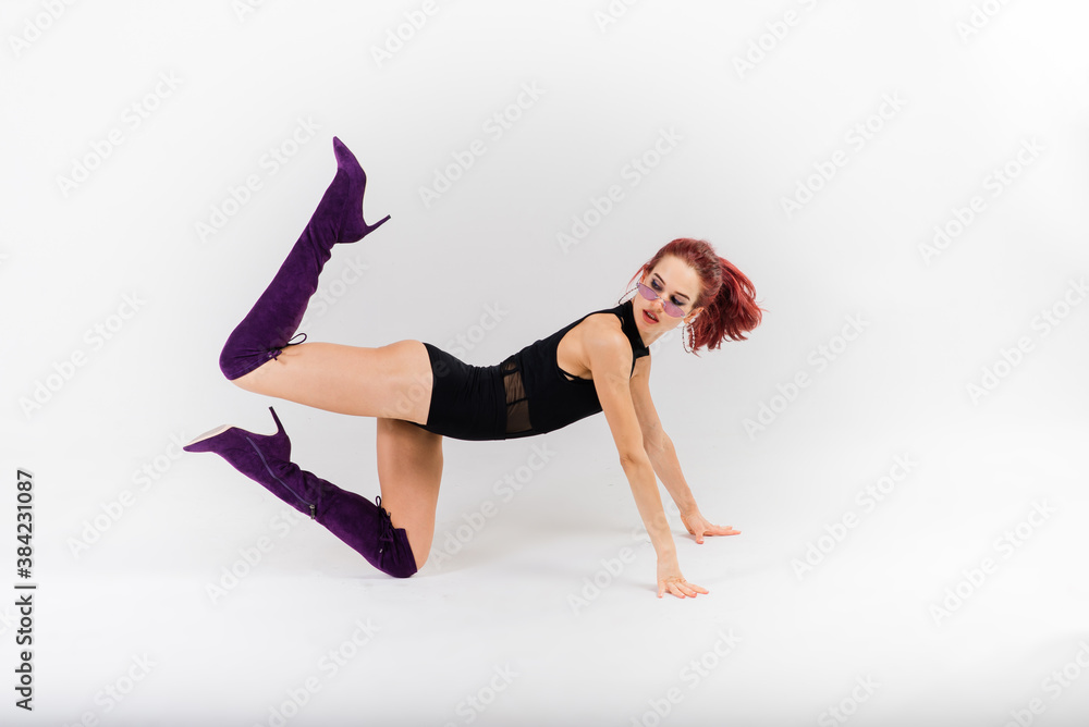 Young beautiful flexible female in black jumpsuit and high heels is posing in a dance studio.
