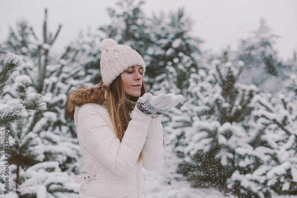 Portrait of happy girl blowing snow in white clothes. Winter forest with snow covered trees. Portrait of happy girl blowing snow in white clothes. Winter forest with snow covered trees.