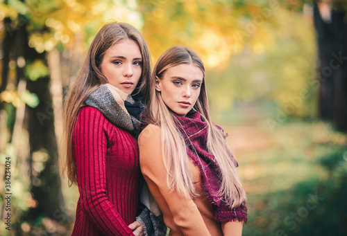 Two young beautiful women in autumn clothes on a background of foliage.