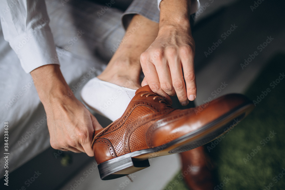 Obraz premium Groom is wearing shoes indoors. Male portrait of handsome guy. Beautiful model boy in colorful wedding clothes. Man is posing