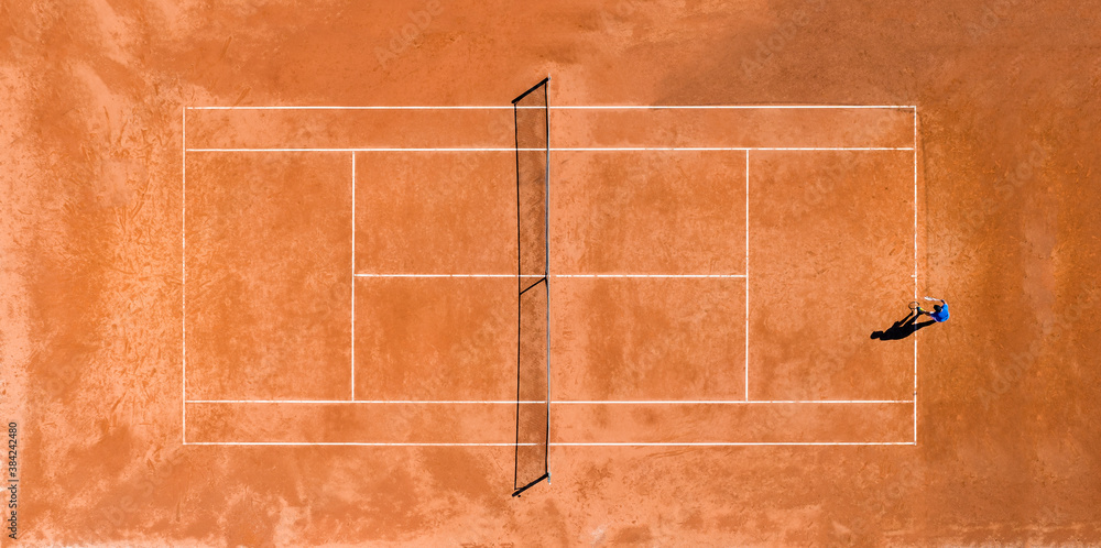 Aerial view of a person playing tennis on a clay court during theCovid-19 outbreak. A clay court is a tennis court that has a playing surface made of crushed stone or other unbound mineral aggregate.