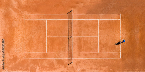 Obraz na płótnie Aerial view of a person playing tennis on a clay court during theCovid-19 outbreak. A clay court is a tennis court that has a playing surface made of crushed stone or other unbound mineral aggregate. w salonie