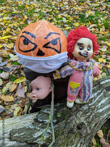 Halloween pumpkin in a disposable mask along with a gang of scary toys against a background of autumn foliage photo