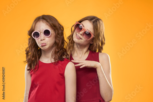 Happy sisters in red dresses on a yellow background are having fun and gesticulating Copy Space © SHOTPRIME STUDIO