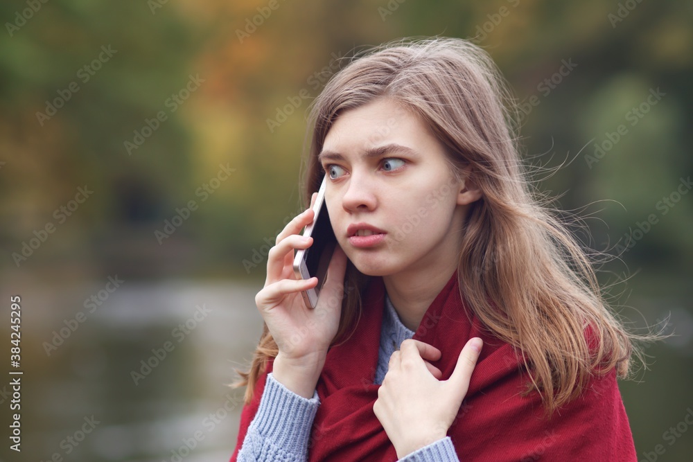 Young frightened scared angry woman talking on her cell mobile smart phone, having negative call, conversation outdoors in park, feeling nervous Young frightened scared angry woman talking on her cell mobile smart phone, having negative call, conversation outdoors in park, feeling nervous