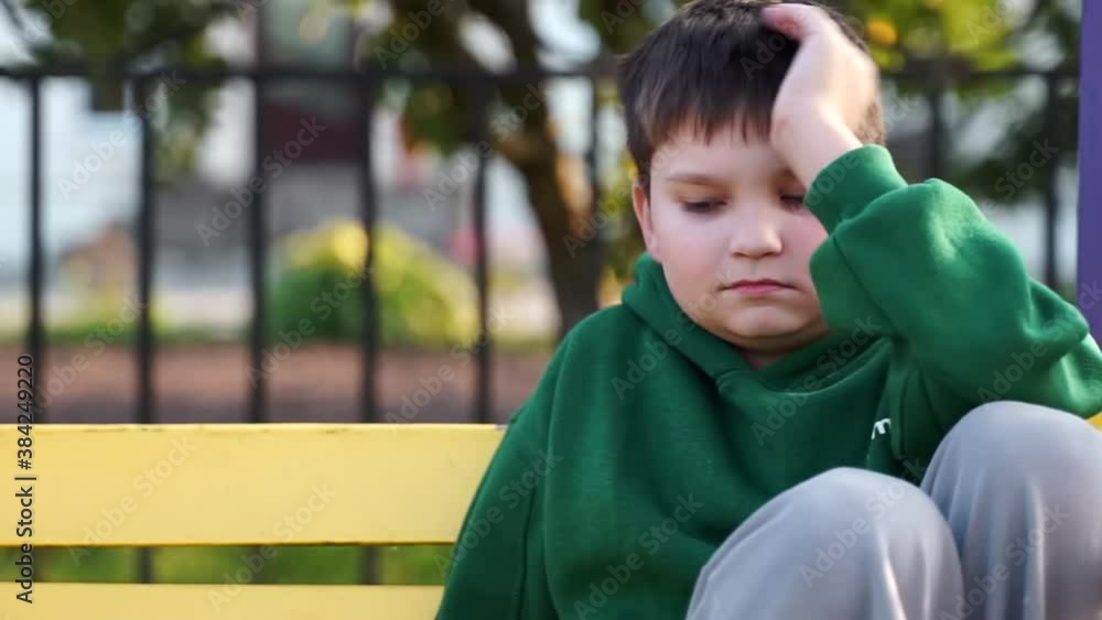 dreamy tired boy child sitting on playground on bench thinking of a problem. disappointed sad young kid looking to camera. bullying at school, depression, loneliness, stress. worried lonely toddler.