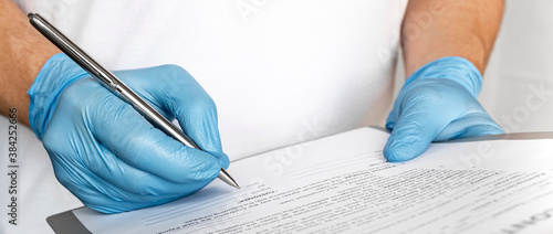 Close-up of professional medical man therapist hands in blue gloves signing medical document on clipboard. Concept of healthcare, medicine and insurance.filling out medical documentation