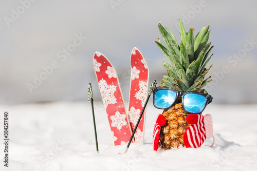 Ripe attractive pineapple in stylish mirrored sunglasses on the snow in the mountain. Winter ski holidays concept. Wearing stylish mittens, sunglass. Sunny day in the mountain. Mountain skiing outfit