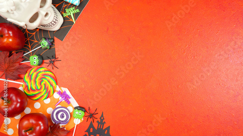 Happy Halloween Trick or Treat theme flat lay with candy and lollipops, skull and pumpkin on textured orange background. Top view blog hero header creative composition with negative copy space.