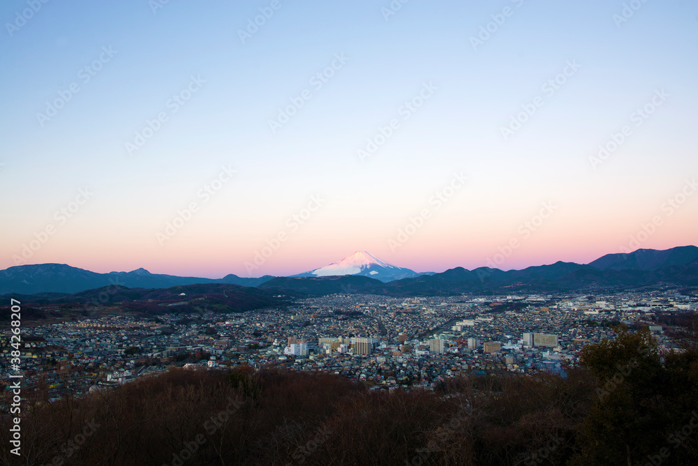 朝日に照らされる富士山と夜明けの街並み
