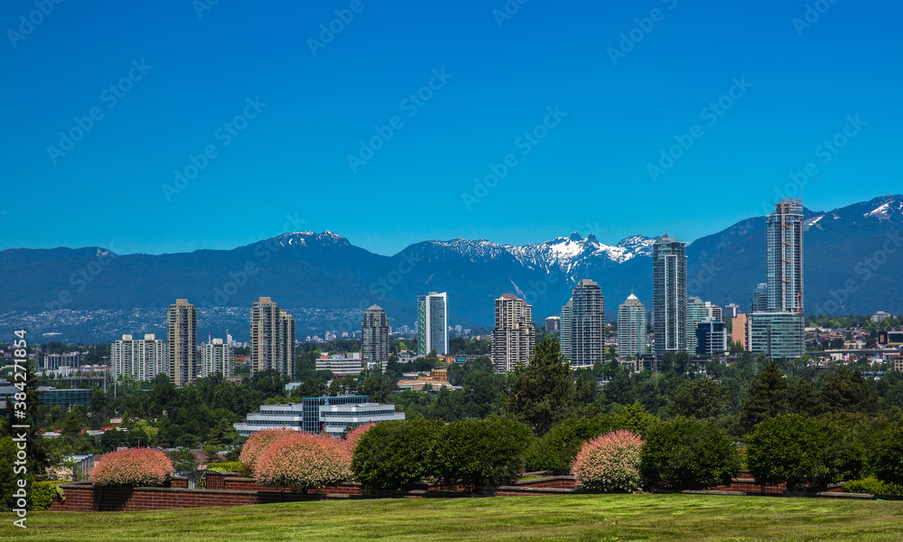 Obraz premium New residential area of high-rise buildings in the city of Burnaby, construction site in the center of the city against the backdrop of snow covered mountain range and blue sky