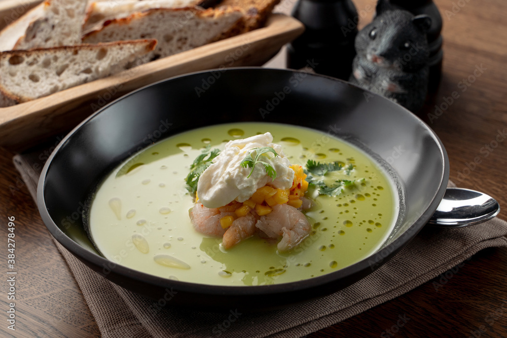 Creamy green soup with crab meat and shrimps on wooden table in a fancy fish restaurant, soft light Creamy green soup with crab meat and shrimps on wooden table in a fancy fish restaurant, soft light