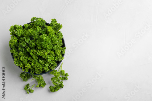 Fresh curly parsley in bowl on light grey table, flat lay. Space for text