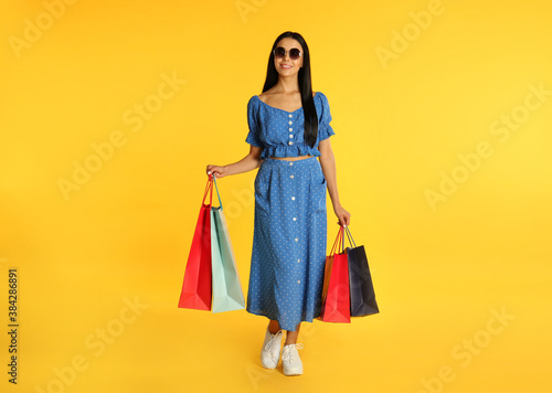 Beautiful young woman with paper shopping bags on yellow background