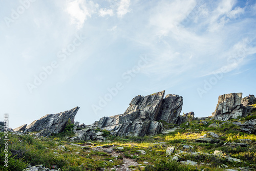 Sunny highland scenery with sharpened stones of unusual shape. Awesome scenic mountain landscape with big cracked pointed stones closeup among grass under blue sky in sunlight. Sharp rocks with cracks