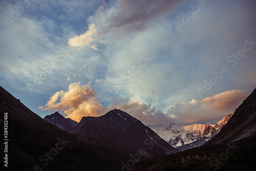 Amazing vivid landscape of sunset with awesome mountain silhouettes and orange clouds. Atmospheric highland scenery with great silhouettes of mountains under dawn sky. Snowy mountains in orange clouds