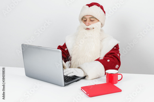 Santa Claus sits at his desk and works at the computer.