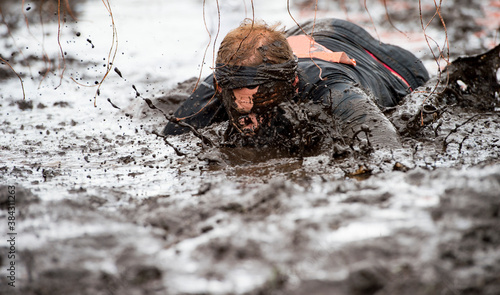 Mud race runners. Crawling,passing under a barbed wire obstacles during extreme obstacle race. Extreame sport concept photo