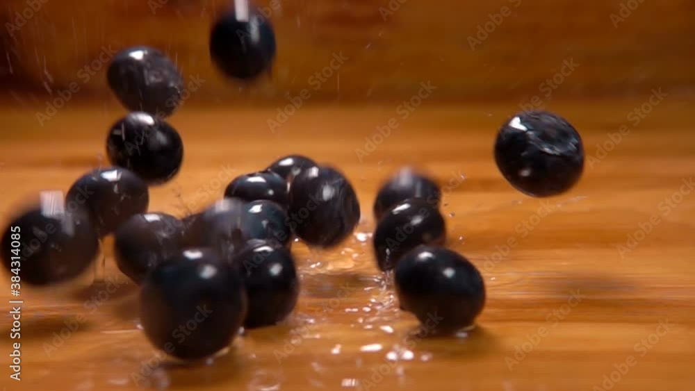 A pile of large blueberries is falling onto the wet wooden surface in slow motion A pile of large blueberries is falling onto the wet wooden surface in slow motion