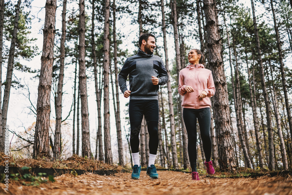 Full length of fit couple running trough woods at autumn and preparing for marathon. - obrazy, fototapety, plakaty 