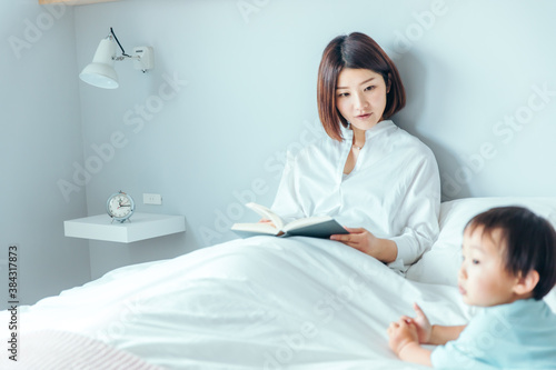 綺麗な白い部屋で女性がベッドで読書しながら子供に話しかけている bed morning