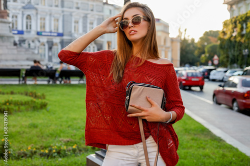 Elegant blond woman in trendy autumn ourfit posing on the street. Wearing sunglasses, sweater and white jeanse. photo