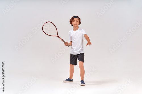 Practicing tennis. Full-length shot of a teenage boy holding tennis racket and looking away isolated over grey background © Kostiantyn