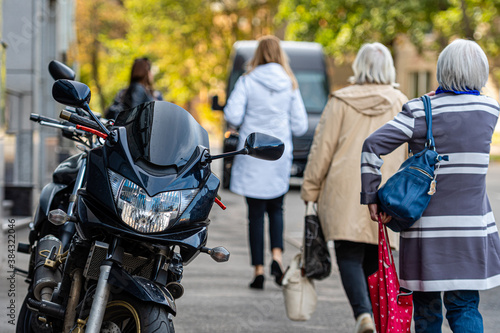 a motorcycle parked on the sidewalk with a defocused pedestrians in the background, selective focus