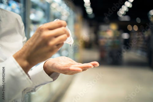 Hands sanitizing against corona virus while shopping in supermarket. Close up view of hands rubbing disinfection to stay healthy. Covid-19 protection measures.
